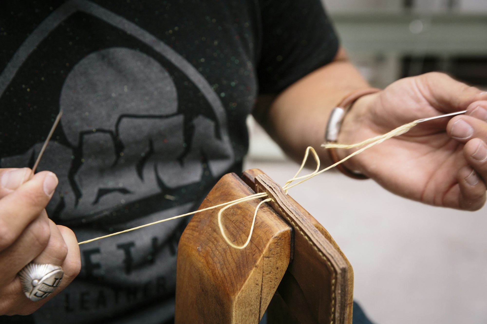 Hands saddle-stitching a leather panel in the workshop